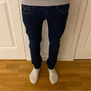 Mörkblå Replay Anbass - Snygga mörkblå jeans från Replay med slim fit (Anbass) och klassisk femficksdesign. Byxorna har en midwaist och är perfekta för en avslappnad stil. De har en dragkedja och knappar framtill. Riktigt feta strl 31/32