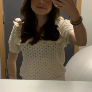 Vit stickad topp med volangdetaljer - Säljer en söt vit  topp med volangdetaljer på axlarna. Jätte fin att ha i vardagen eller på finare tillfällen 