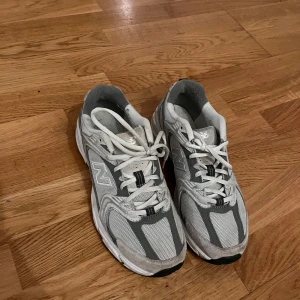 Grå och vita sneakers från New Balance - Säljer ett par grå och vita sneakers från New Balance. Skorna har en klassisk design med snörning och en bekväm passform. Perfekta för vardagsbruk och träning.
