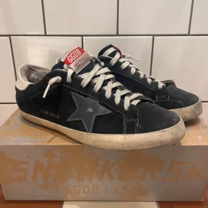 Svarta sneakers från Golden Goose - Snygga svarta sneakers från Golden Goose med vit sula och stjärndetalj på sidan. Skorna har snörning och en röd etikett på plösen med GGDB-logga. Perfekta för en avslappnad stil.
