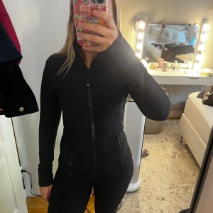 Lululemon träningsjacka  - Säljer en svart, figursydd träningsjacka från Lululemon med dragkedja framtill och två fickor med dragkedja. Storlek 6 vilket motsvarar en xs/s. Använd ca 2 gånger. Köp på NK och har kvitto kvar!