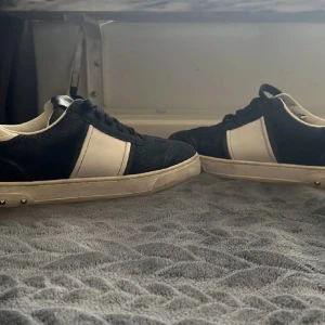 Valentino Garavani sneakers svart/vit - Snygga sneakers från Valentino Garavani i svart mocka och vitt skinn. Klassisk låg modell med snörning och coola nitar längs sulan. Perfekta för dig som vill ha en stilren men edgy look. Tydlig Valentino-logga på sulan.