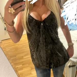 Svart paljettlinne med smala axelband - Glittrigt svart linne med paljetter och smala axelband. Djup v-ringning framtill och lätt a-linjeformad passform.💕 perfekt till fester och kvällar ute!