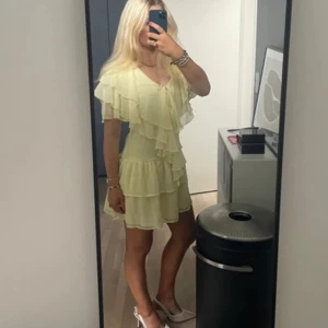 Ljusgul volangklänning med kort ärm - Supersöt ljusgul kortklänning med flera lager volanger och v-ringning. Klänningen har korta ärmar och är tillverkad i ett lätt, flowy material som ger en luftig känsla. 