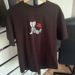  Off-White t-shirt  - Cool svart t-shirt från Off-White med färgglatt graffiti-inspirerat tryck av en KAWS-liknande figur på både bröstet och ryggen. Klassisk passform och korta ärmar. Materialet är mjuk bomull som känns skönt mot huden. Perfekt för dig som gillar streetwear och unika prints. Storlek M, pris kan diskuteras 