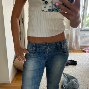 Blå bootcut jeans med låg midja - Säljer ett par blå jeans med snyggt slitna detaljer, låg midja och bootcut-ben. Jeansen har dubbla knappar i midjan och klassiska fickor fram och bak. Storlek står inte tyvärr men midjemåttet är 37 cm