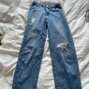 Blå raka jeans med slitningar - Säljer ett par blå jeans med raka ben och snygga slitningar på låret och knät. 