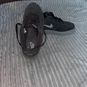 Nike Air Force 1 i svart mocka - Snygga Nike Air Force 1 sneakers i svart mocka med silverfärgad swoosh och grå sula. Klassisk låg modell med snörning och rund tå. Perfekta för dig som gillar stilrena och tidlösa sneakers med en twist. Passar bra för vinter använd 5 gånger köpt för 1200 säljer de eftersom jag har köpt nya skor 