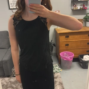 Svart ärmlös blus med spetsdetaljer - Säljer en svart ärmlös blus med snygga spetsdetaljer över axlarna.💕