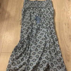 Blå långkjol med mönster och snörning - Långkjol i ljusblått med mörkblått och vitt mönster. Smockad upptill och dekorativ snörning med tofsar framtill. Luftigt material, perfekt för varma dagar. Använd fåtal gånger förra sommaren (2024) 💕Minns inte nypris