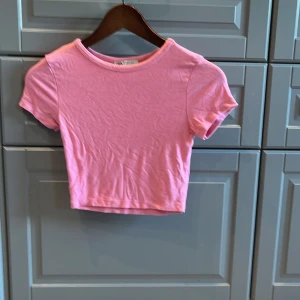 Rosa croppad topp från Zara - Säljer en söt rosa magtröja croppad topp från Zara. T-shirten har korta ärmar, rund halsringning och är tillverkad i mjuk bomull. Perfekt för dig som gillar en enkel men trendig stil. Passar till både jeans och kjol! Som passar för ungre 