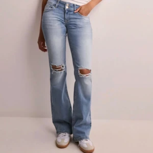 Ljusblå bootcut jeans med slitningar - Säljer ett par ljusblå lågmidjade bootcut jeans med snygga slitningar över knäna och stängbara fick där bak! Använt en del men är i jättefint skick, har sytt upp de lite på längden, jag är 163 och de går precis ner till marken nu!🥰Väldigy stretchiga