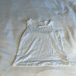 Vit linnetopp från Lindex Kids - En klassisk vit linnetopp från Lindex Kids i mjuk bomull. Modellen är ärmlös med rund halsringning och raka linjer, perfekt för en enkel och clean look. Passar till allt och är superbekväm att bära under varma dagar.