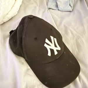 Svart New York Yankees keps - Svart keps från New Era med klassiskt New York Yankees-logo broderat i vitt framtill. Justerbar rem baktill för perfekt passform. Snygg och sportig stil som passar till det mesta. Materialet är bomull och kepsen har böjd skärm.
