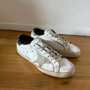 Golden Goose skor - Golden Goose sneakers i vitt skinn med grå mockadetaljer och ikonisk stjärna på sidan. Skorna har snörning, rund tå och platt sula. Hälpartiet har ett unikt mönster i grönt och beige. Perfekta för dig som gillar en avslappnad och trendig look.
