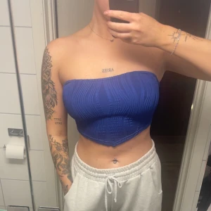 Blå bandeau tubtopp med snörning - Säljer en blå bandeau tubtopp med snygg snörning i ryggen. Toppen har en lätt ribbad struktur och sitter tight över bysten. Perfekt för dig som vill ha en trendig och stilren look till sommaren.