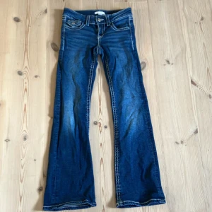 Blå bootcut jeans Gina Tricot 146 - Snygga blå jeans från Gina Tricot i storlek 146. Modellen har bootcut-ben, klassiska fickor med lock och markerade vita sömmar. Jeansen har låg midja och är tillverkade i mjukt denimtyg med lätt slitning för en cool look.