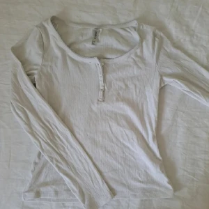 Vit ribbad långärmad tröja - Säljer en vit ribbad långärmad tröja från lindex. Tröjan har rund halsringning och knappar framtill, vilket ger en enkel men snygg look. Perfekt att matcha med jeans eller kjol för en chill stil.