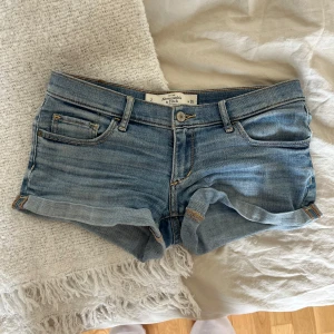Lågmidjade jeansshorts Abercrombie - Snygga lågmidjade jeansshorts från Abercrombie & Fitch i ljusblå denim. Klassisk femficksmodell med uppvikta benslut och coola detaljer på bakfickorna. Perfekta för varma sommardagar och enkel att matcha med allt.