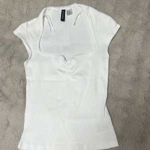 Vit ribbad topp  - Vit ribbad topp från H&M med korta ärmar och dekorativ kant och knytband. Priset kan diskuteras 
