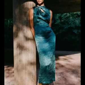 Elegant Maxiklänning Från Zara - EJ ANVÄND! Snygg grön ärmlös klänning med en elegant drapering framtill och en liten slits bak. Perfekt för en stilfull kväll. Klänningen har en unik knytdetalj vid halsen. Mått: Storlek S  Bröst: 38.0.  Midja: 34.0.  Höft: 46.0 Framsidan längd: 132,5. 