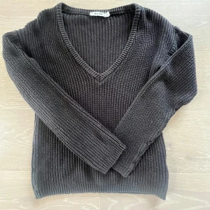 Svart stickad v-ringad tröja NA-KD - Mysig svart stickad tröja från NA-KD i storlek XXS. Tröjan har v-ringning, ribbade muddar och lång ärm. Perfekt för lager-på-lager och chill dagar. Enkel att matcha med jeans eller kjol för en clean look.