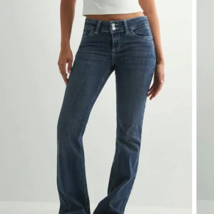 NELLY JEANS - Snygga mörkblå bootcut jeans med klassisk femficksdesign och coolt vitt broderi på bakfickorna. Jeansen har medelhög midja och är tillverkade i stretchig denim för en bekväm passform. Perfekta till sneakers eller boots.