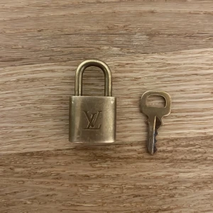 Louis Vuitton hänglås med nyckel - Säljer ett klassiskt Louis Vuitton hänglås i mässing med tillhörande nyckel. Låset har LV-loggan på framsidan och märkning på baksidan. Perfekt accessoar till din LV-väska eller som samlarobjekt. Modellen är MINI. Självklart äkta. Inga tillbehör eller OG följer med. 