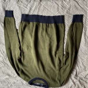 Olivgrön stickad tröja Dressmann M - Olivgrön stickad tröja från Dressmann i storlek M. Tröjan har mörkblå ribbade muddar vid hals, ärmslut och nederkant. Perfekt för lager-på-lager och chill höst- eller vinterstil.