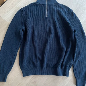 Marinblå stickad half zip från Zara - Säljer en marinblå stickad tröja från Zara med ribbad struktur och half zip-dragkedja i halsen. Tröjan har lång ärm och hög krage, perfekt för lager-på-lager. Snygg och enkel att matcha till olika outfits.
