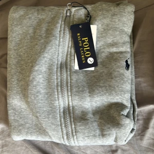 Grå zipjacka från Polo Ralph Lauren - Snygg grå zipjacka från Polo Ralph Lauren med klassisk broderad logga på bröstet. Jackan har hel dragkedja. Perfekt för en chill och stilren look.( vet ej om den är äkta)