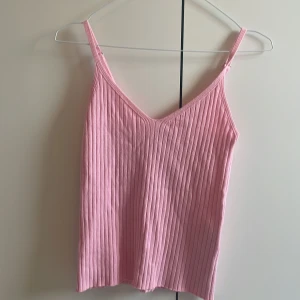 Rosa ribbad linnetopp - Säljer en ljusrosa ribbad linnetopp med smala axelband och v-ringning. Toppen är ärmlös och har en mjuk, stretchig känsla som gör den superbekväm. Perfekt för varma dagar eller att styla lager på lager.