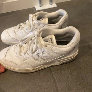 Vita New Balance 550 skor - Säljer ett par klassiska New Balance 550 sneakers i helvitt skinn med snygga detaljer och broderad logga. Inga fläckar, skorna är som nya och endast använda någon gång.  (Kan finnas någon liten crease) Perfekta för dig som gillar stilrena och trendiga sneakers.