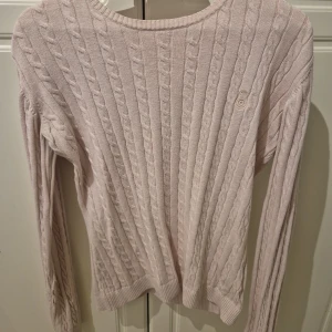 Ljusrosa kabelstickad tröja Sail Racing - Supersöt ljusrosa kabelstickad tröja från Sail Racing. Tröjan har rund halsringning, långa ärmar och diskret logga broderad på bröstet. Perfekt för dig som gillar klassisk och clean stil. Materialet är mjukt och skönt, passar till många outfits.