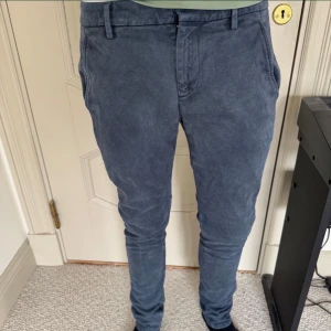 Blå chinos från Dondup, stl 29 - Snygga blå chinos från Dondup i storlek 29. Byxorna har slim passform, klassiska sidofickor och bakfickor med knapp. Materialet är mjukt och bomulligt, perfekt för en clean och stilren look. Metall-D vid bakfickan ger en extra detalj. Nypris 3500kr. Byxorna är använda med hänsyn och är i väldigt gott skick