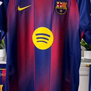 FC Barcelona Lamine Yamal #10 fotbollströja - Säljer en officiell FC Barcelona matchtröja med Lamine Yamal och nummer 10 på ryggen. Tröjan är blå och röd med gula detaljer, klubbmärke, Nike-logga och Spotify som sponsor framtill. Champions League och UEFA Foundation badges på ärmen. Tillverkad i lätt och ventilerande material.