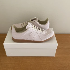 Maison Margiela  sneakers beige/vit mocka - Maison Margiela  sneakers i ljusbeige/vit mocka med klassisk gummisula. Snygg minimalistisk design med ton-i-ton snörning och diskret branding på plösen och sulan. Perfekta för dig som gillar stilrena och trendiga sneakers. Använda några gånger. Säljer för att de inte var i min storlek, dustbag och en något defekte rad låda kommer med.