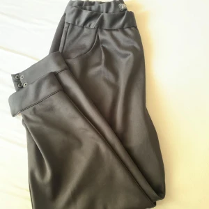 Svarta byxor från Zara - Svarta byxor från Zara med elastisk midja och raka ben. Byxorna har diskreta fickor och stilrena detaljer vid benslutet. Perfekta för en clean och snygg look. Materialet är mjukt och har en lätt glansig finish.