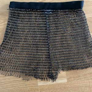 Glittrig nätkjol från Missy Empire - Glittrig svart nätkjol från Missy Empire i storlek M. Kjolen är kort och består av ett transparent nät med små silverfärgade pärlor och stenar över hela tyget. Perfekt för att sticka ut och skapa en edgy look.