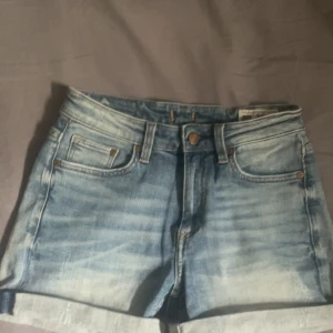 Ljusblå jeansshorts från Crocker - Snygga ljusblå jeansshorts från Crocker med klassisk femficksdesign och uppvikta benslut. Shortsen har normal passform och är tillverkade i slitstarkt denim med snygga slitningar och detaljer i kopparfärg. Perfekta för varma dagar och enkel att matcha med allt.