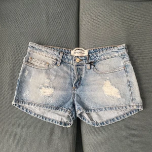 Blå slitna jeansshorts från Canyon - Snygga ljusblå jeansshorts från Canyon Jeans med slitna detaljer framtill och bak. Klassisk femficksmodell, normal passform och råa kanter. Perfekta för sommardagar 