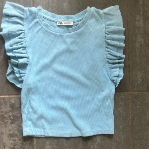 Blå volangärmad topp från Zara - Supersöt ljusblå topp från Zara med volangdetaljer på ärmarna. Modellen är croppad och har en ribbad struktur som ger en trendig känsla. 
