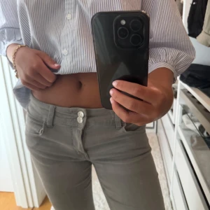 Grå bootcut jeans med låg midja - Snygga grå jeans med bootcut-modell och låg midja. Byxorna har två knappar framtill, klassiska bakfickor. 