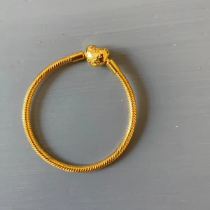 Pandora armband  - Snyggt armband i guldton med ett hjärtformat lås. Armbandet har en klassisk, vriden design och är perfekt för att matcha med andra smycken. Hjärtat ger en söt och trendig touch som sticker ut. Längd 16 cm  