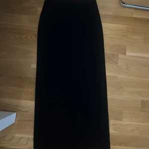 Svart långkjol i enkel stil - En stilren svart långkjol med rak passform. Kjolen är helt enfärgad och har en klassisk look som är lätt att matcha med olika toppar och skor. Perfekt för dig som gillar minimalistisk och tidlös stil. Aldrig använd