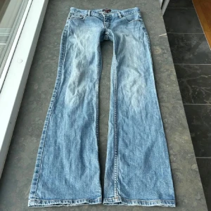Ljusblå bootcut jeans - Snygga ljusblå jeans från Oasis med bootcut-modell och klassisk femficksdesign. Jeansen har dekorativa sömmar på bakfickorna. Perfekta för dig som gillar en retro vibe och vill ha ett par jeans med lite extra vidd nertill. Bilderna är lite gamla, de har ett hål på knäet nu, men kan klippas upp till ett större men inget fult o ba lämna där; men där av priset. 38cm midje mått 79 innerbens längd