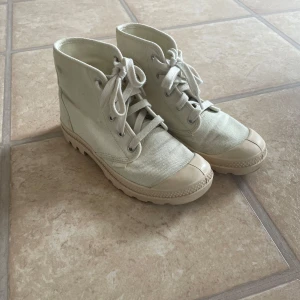 Beige Palladium boots i canvas, strl 37 - Snygga beige boots från Palladium i canvas med klassisk snörning och robust sula. Skorna har rund tå och är perfekta för dig som gillar en avslappnad men cool stil. Passar till både jeans och shorts för en urban vibe. Sparsamt använda.