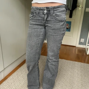 Grå bootcut jeans med dubbla knappar - Säljer ett par grå jeans med snygg tvätt, bootcut-modell och dubbla knappar i midjan. Jeansen har klassiska fickor fram och bak, samt coola söm-detaljer. Perfekta för dig som gillar en avslappnad men trendig look.