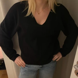 Svart v-ringad stickad tröja - En svart stickad tröja med v-ringning och långa ärmar. Tröjan har en enkel och stilren design som passar perfekt till jeans. Mjuk och skön att bära, med en lite loose passform.