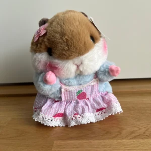 Söt rosa hamster med jordgubbklänning - Supergullig hamster i en klänning i rosa och vitt med ränder och små jordgubbar, spetskant och rosett i nacken. Söt kawaii-stil nallebjörn importerad från Japan. Märke: Momoco.